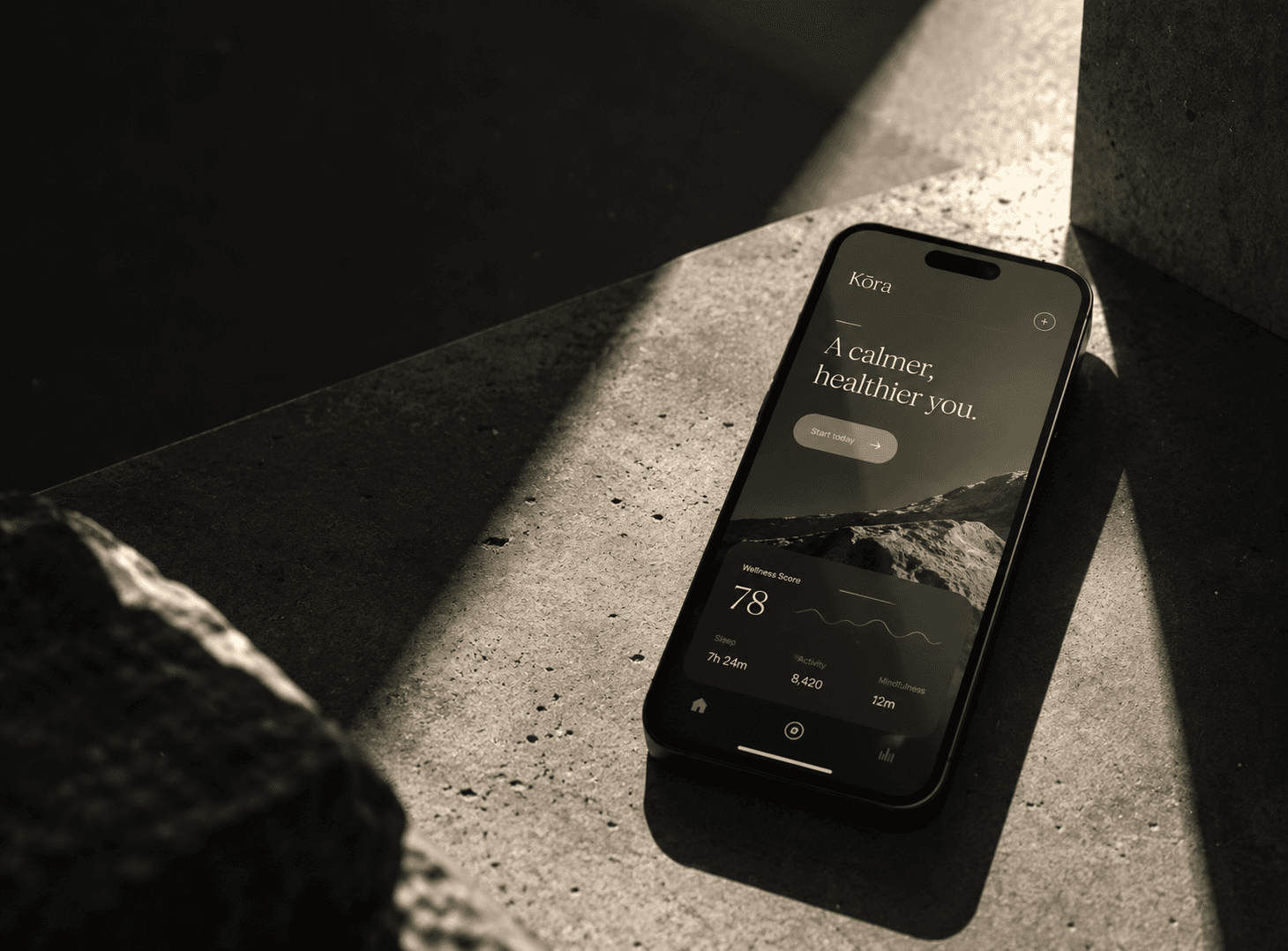 Phone showing the Kōra Health app home screen with a wellness score, resting on warm concrete in low sunlight